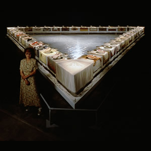 Judy Chicago standing with the Dinner Party